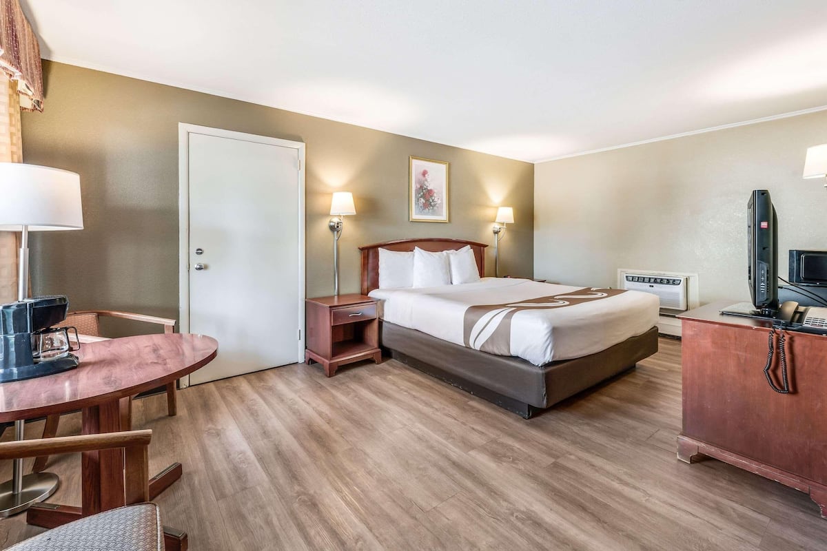 Una habitación de hotel con cama, mesita de noche, lámpara, escritorio, silla y televisor.