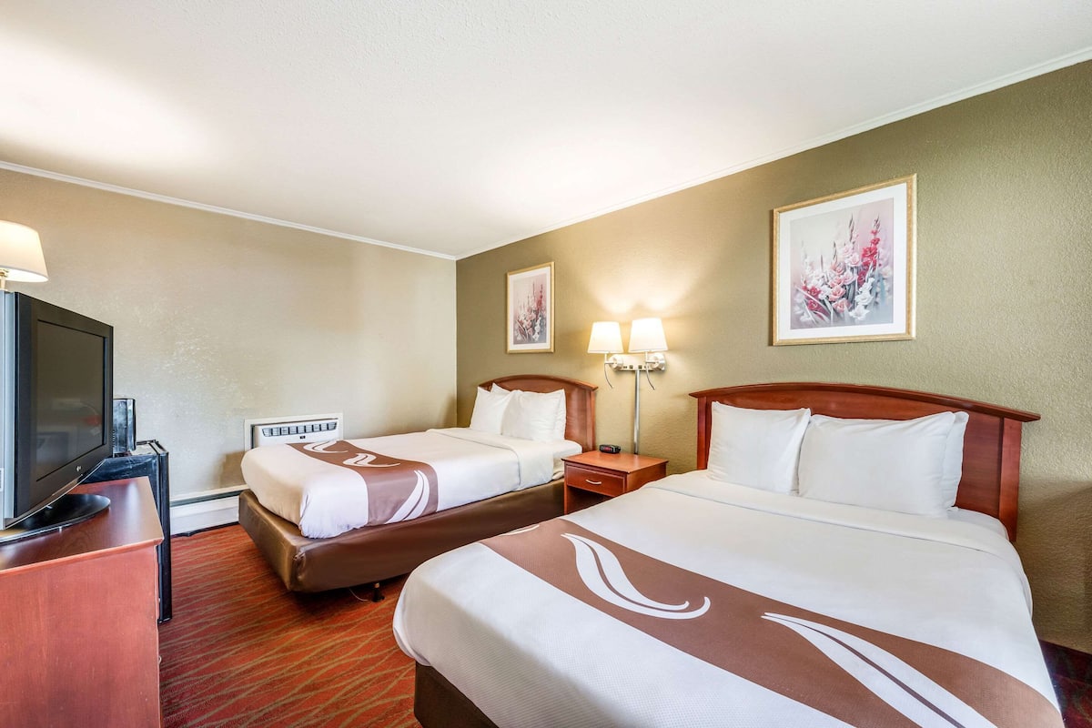 Una habitación de hotel con dos camas, televisión, escritorio y lámpara.