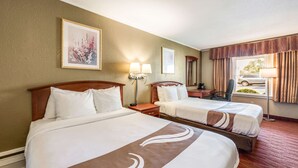 Habitación de hotel con dos camas, una mesita de noche, una lámpara y una ventana con cortinas.