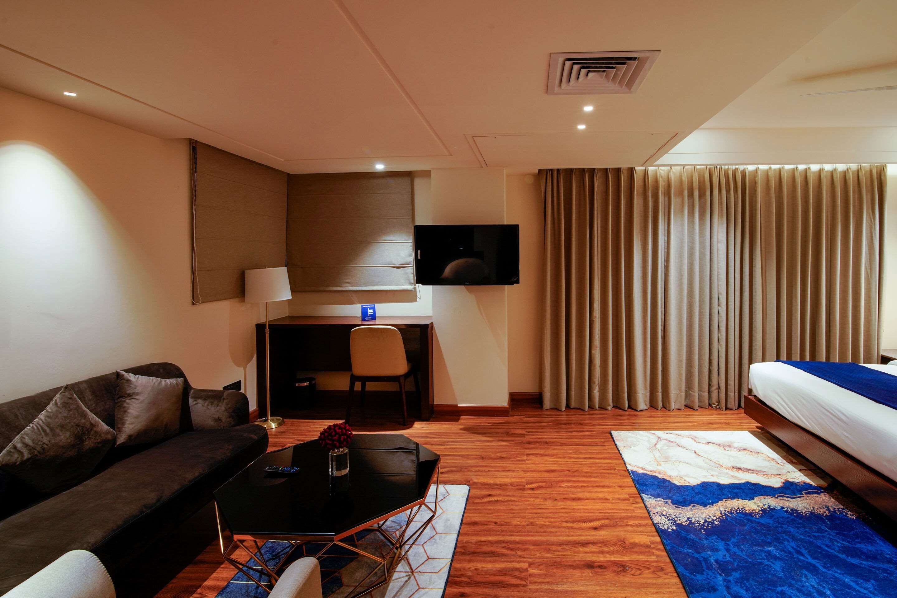 Une chambre d’hôtel équipée d’un canapé, d’un bureau, d’une télévision, d’un lit et d’une fenêtre avec des rideaux.