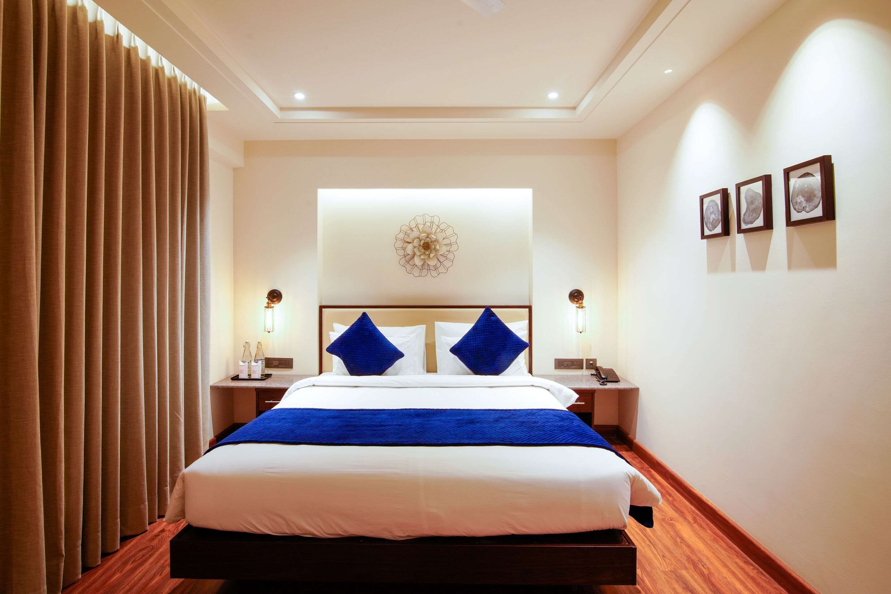 Una habitación de hotel con una cama grande, una mesita de noche con lámpara, una obra de arte en la pared y una ventana con cortinas.