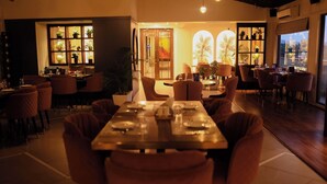 En restaurant med et langt træbord dækket til spisning, omgivet af polstrede stole.