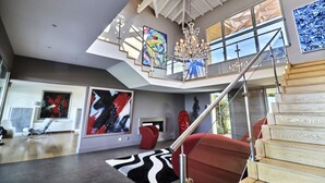 Un amplio salón con techo alto, una escalera y obras de arte moderno.