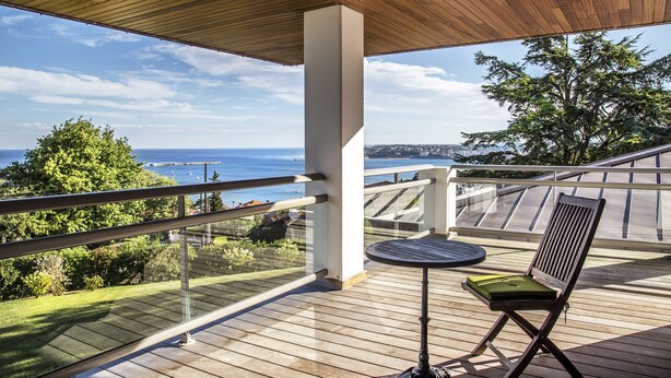 Una terraza de madera con una mesa y una silla, con vistas a un paisaje escénico del océano y la vegetación.