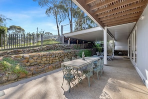 An outdoor patio with a stone wall, a table with chairs, and a covered area with a pergola.