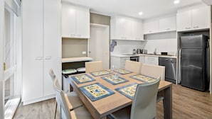 A modern kitchen with white cabinets, a dining table with chairs, and a refrigerator.