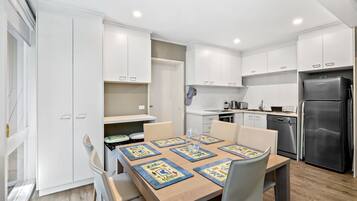 Une cuisine moderne avec des meubles blancs, une table à manger avec des chaises et un réfrigérateur.