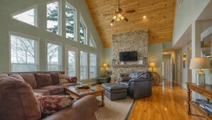 A spacious living room with a stone fireplace, leather furniture, and large windows. - Cozy Cabin with Mountain Views, Pet Friendly, 3 Miles from Downtown Highlands (Highlands)