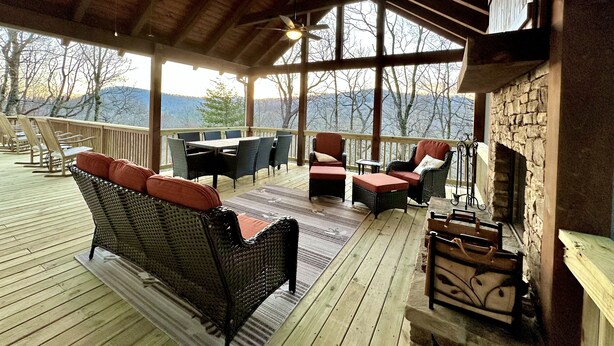 A covered outdoor deck with wicker furniture, a stone fireplace, and a view of the mountains. - Cozy Cabin with Mountain Views, Pet Friendly, 3 Miles from Downtown Highlands (Highlands)