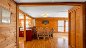 Un intérieur en bois comprenant un coin repas avec une table et des chaises, un coin cuisine avec des placards rouges et une porte en bois.