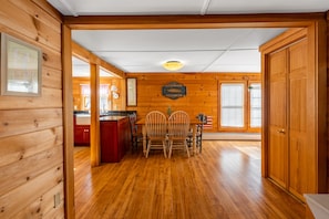 Un intérieur en bois comprenant un coin repas avec une table et des chaises, un coin cuisine avec des placards rouges et une porte en bois.