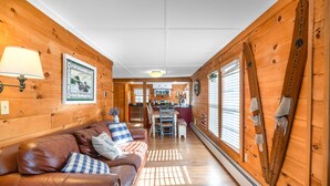Un intérieur de chalet chaleureux avec un canapé en cuir, des murs en bois, un coin repas et du matériel de ski.