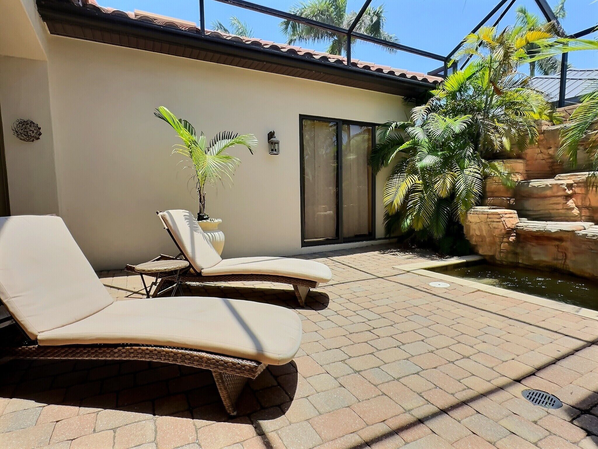 Eine Terrassenfläche mit zwei Loungestühlen, einer Topfpflanze und einem Wasserspiel.