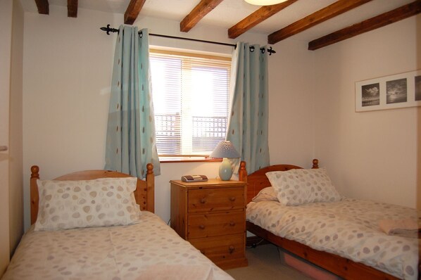 A bedroom with two wooden beds, a nightstand with a lamp, and a window with curtains.