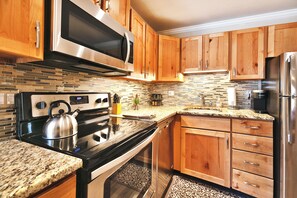 Una cocina moderna con armarios de madera, electrodomésticos de acero inoxidable, encimera de granito y salpicadero decorativo.