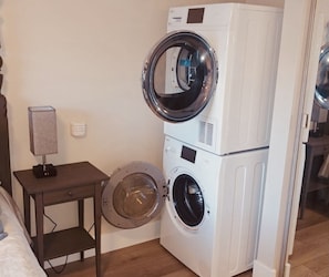 A stacked washer and dryer unit in a room with a small table and lamp. - Carriage House 1BR | Ski Slope Views | Fireplace | Pool & Hot Tub (Park City)