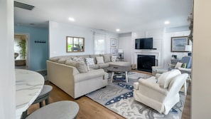 A living room with a sofa set, a fireplace, a television, and a dining area with a table and chairs. - Overlook the Cailbogue Sound On Your Private Deck (Hilton Head Island)