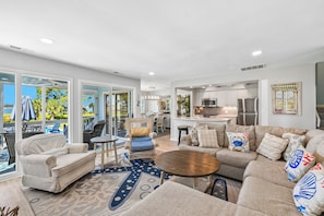 A spacious living area with a large sofa, a coffee table, and a dining table. There is a kitchen area with modern appliances and a view of the outdoors. - Overlook the Cailbogue Sound On Your Private Deck (Hilton Head Island)