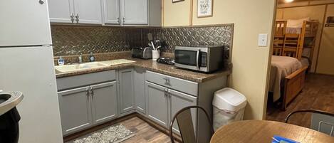 A compact kitchen with a refrigerator, microwave, and sink. There is a dining table with chairs and a rug on the floor.