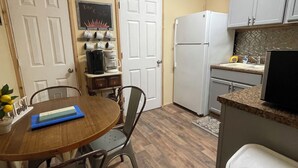 Une cuisine compacte équipée d’un réfrigérateur, d’un four à micro-ondes et d’un évier. On y trouve une table à manger avec des chaises et un petit meuble de rangement.