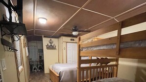 Une petite chambre comprenant un lit superposé, un lit simple, un bureau en bois et un ventilateur de plafond.
