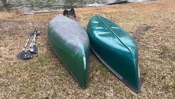 Two green kayaks and a paddle on a grassy area near a body of water.