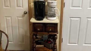 Un coin café avec un tableau noir sur lequel est écrit « Réveillez-vous et profitez de la journée », une machine à café, un mousseur à lait et un porte-tasses avec des tasses étiquetées.
