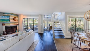 Ein geräumiges Wohnzimmer mit Kamin, großem Fenster und einer Treppe, die in ein Obergeschoss führt.
