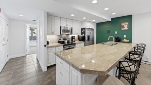 A modern kitchen with white cabinets, stainless steel appliances, a granite countertop, and a green accent wall. - Keystone Condo in Quiet Location w/ Private Balcony for Great Mountain Views (Keystone)