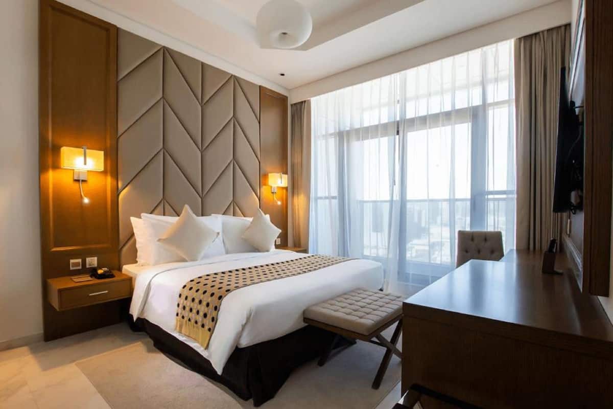 A hotel room with a large bed, two bedside lamps, a desk, and a chair.