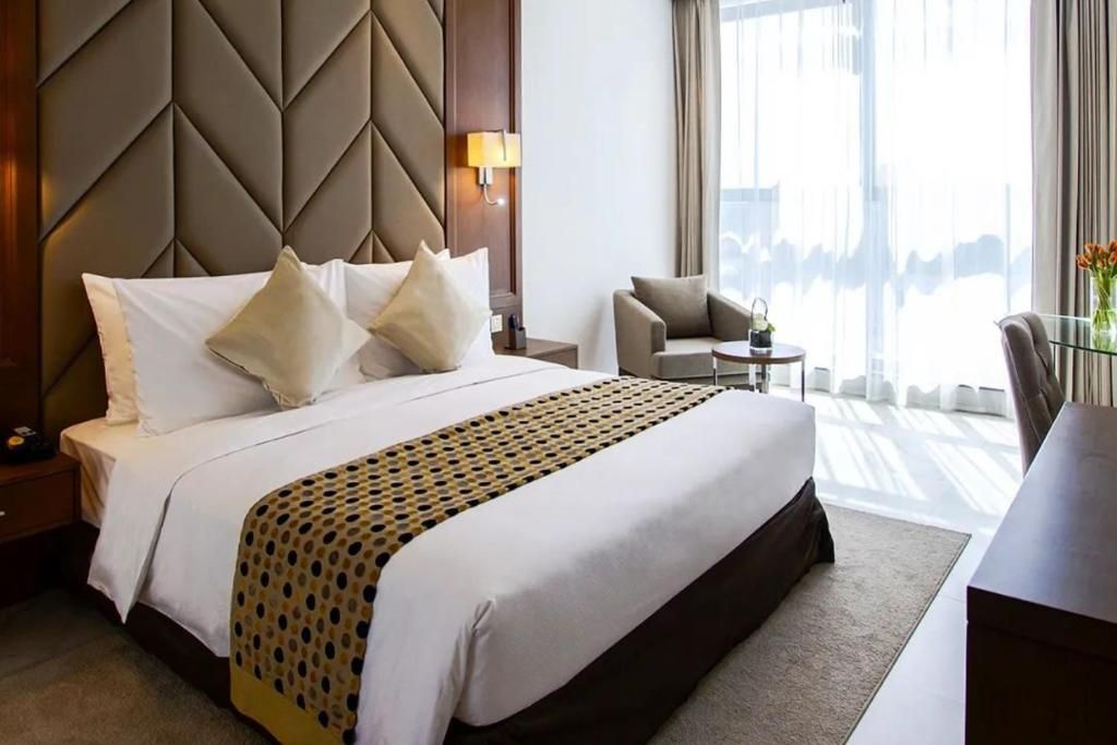 Habitación de hotel con una cama grande, una mesita de noche, una silla, una pequeña mesa y vistas al exterior.