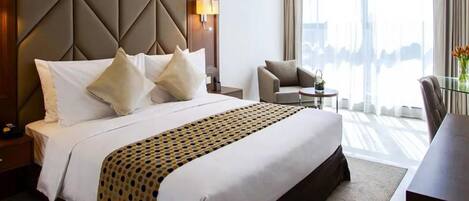 Habitación de hotel con una cama grande, una mesita de noche, una silla, una pequeña mesa y vistas al exterior.