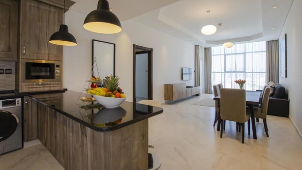 Cozinha moderna com ilha central, área de refeições com mesa e cadeiras, e sala de estar com sofá e televisão.