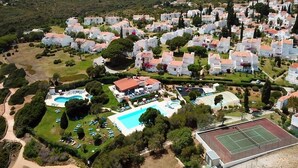 Vista aérea de una zona residencial con casas blancas, una piscina y una cancha de tenis.