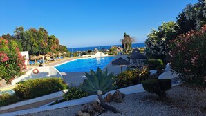 Vista a la piscina con una vista despejada del océano, sillas de descanso y un jardín bien cuidado.