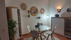 Un comedor con una mesa redonda de vidrio, sillas blancas y un armario de madera.