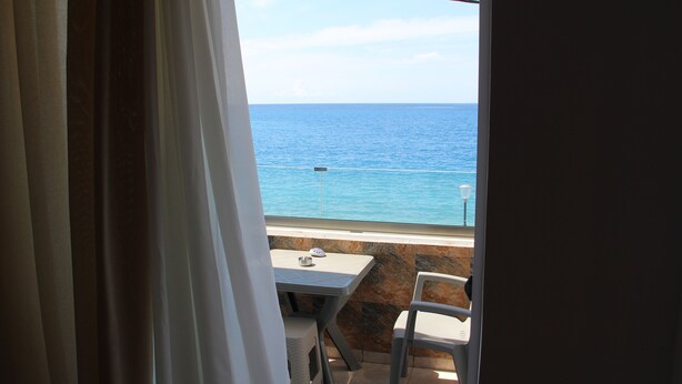 Un balcón con mesa y silla, con vista a un mar azul y despejado.