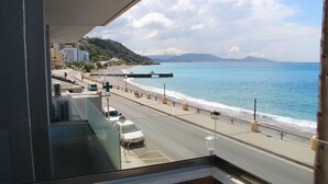 Vista desde un balcón sobre una carretera costera, con una playa y montañas al fondo.