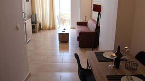 Una sala de estar moderna con un sofá, una mesa de comedor para dos personas y una cocina al fondo.