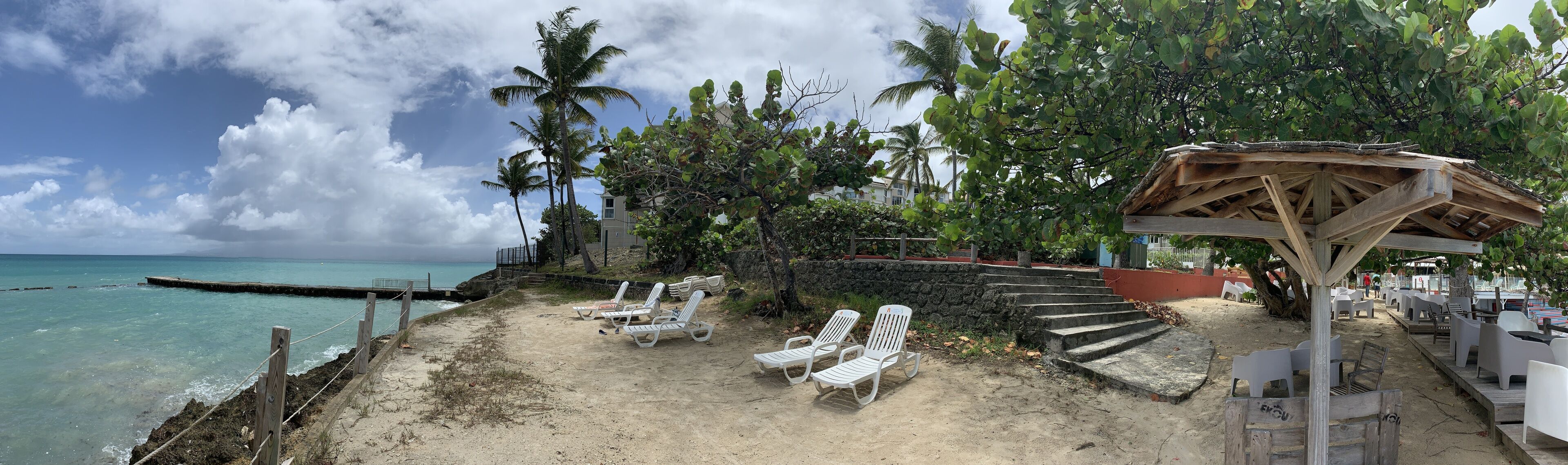 A beach with white lounge chairs, a wooden structure, and a view of the ocean.