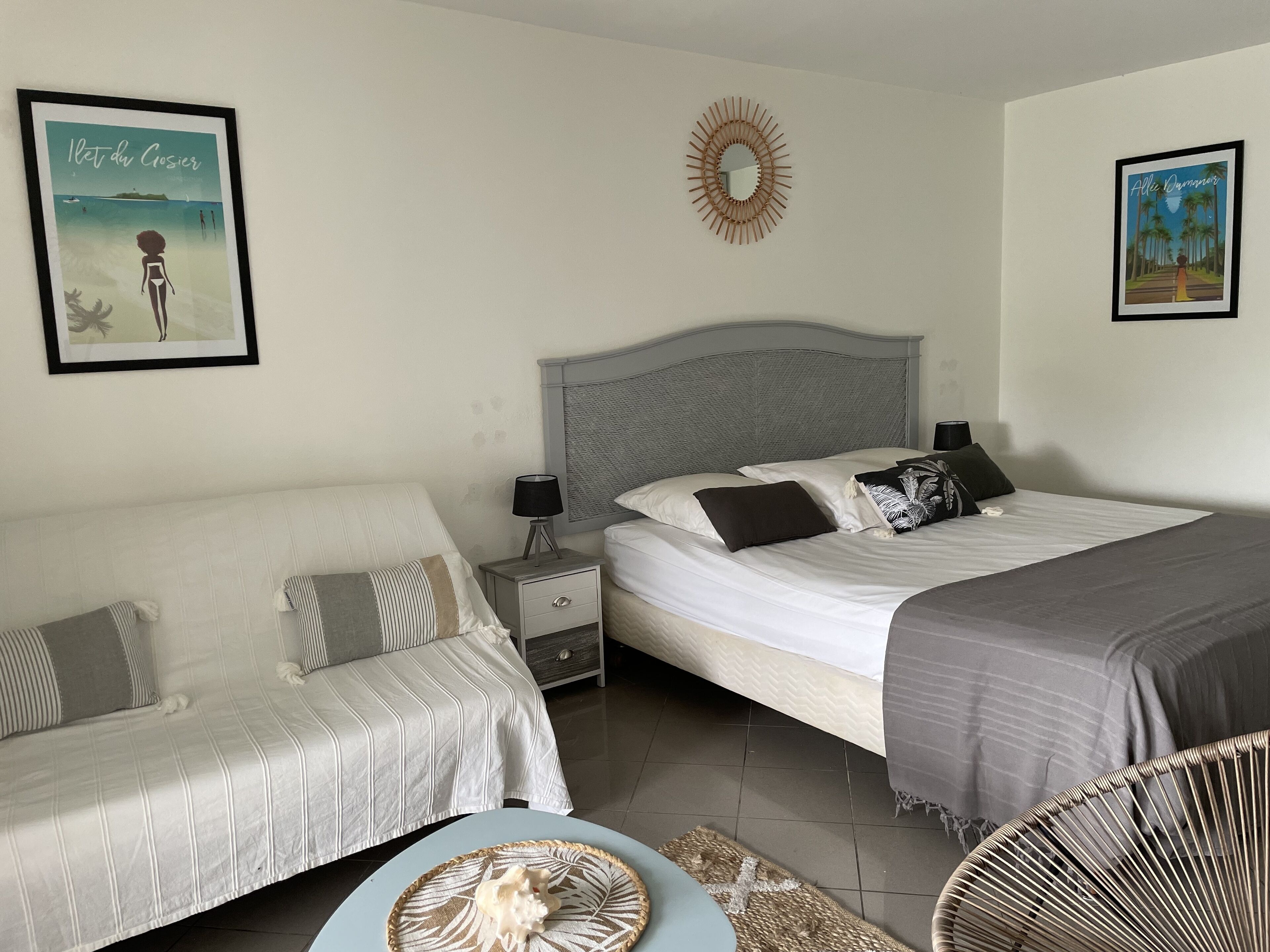 A bedroom with a bed, a bedside table, a nightstand, a chair, and two framed pictures on the wall.