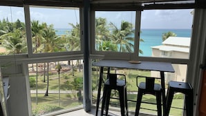Un balcon avec une table et des chaises, offrant une vue sur l’océan et les palmiers.