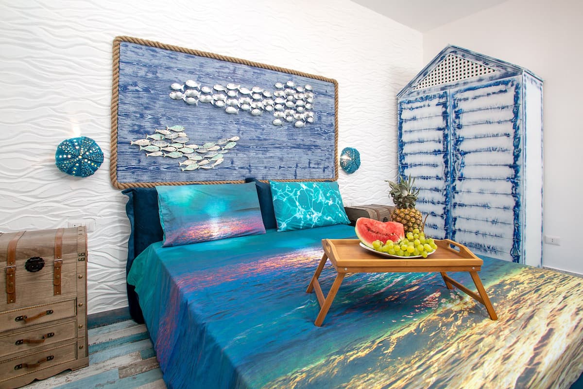 A bedroom with a bed, a wooden chest, a headboard with a fish design, and a fruit tray on the bed.