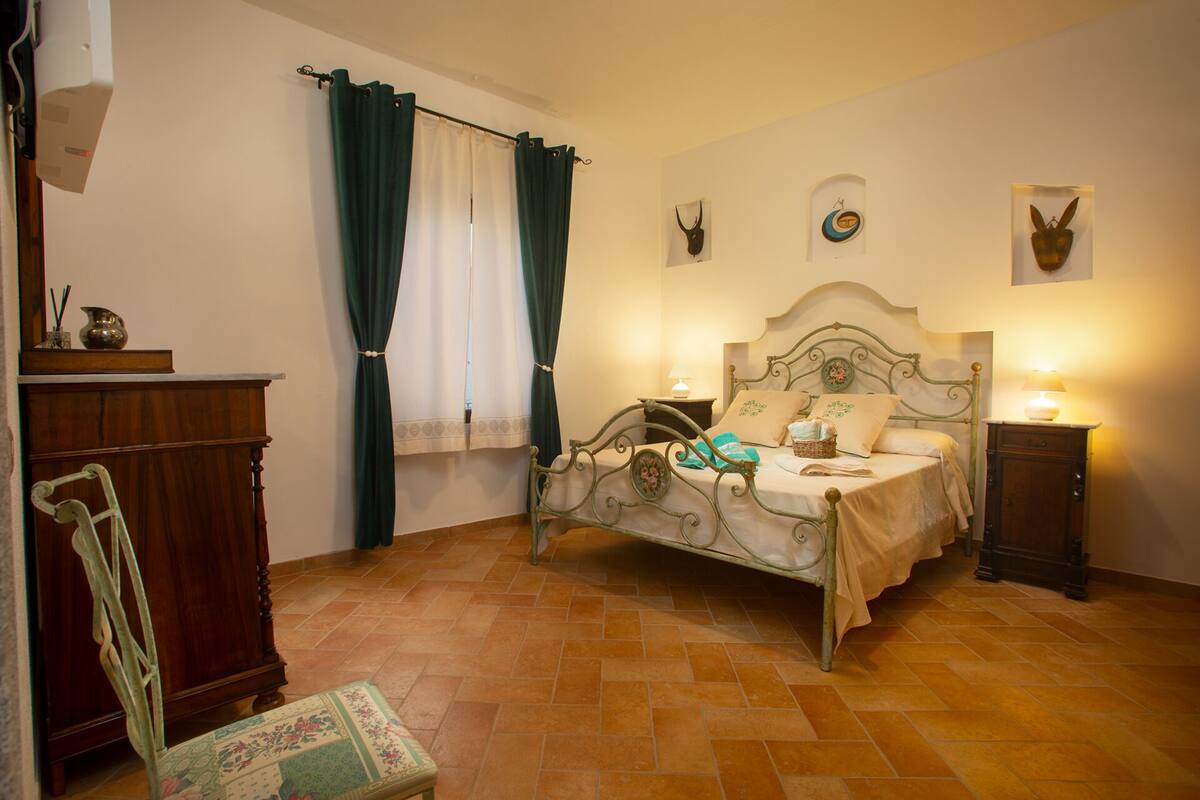 A bedroom with a bed, a nightstand, a dresser, a chair, and a window with curtains.