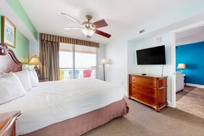 Une chambre d’hôtel avec un grand lit, un ventilateur de plafond, un téléviseur à écran plat, une commode et un balcon équipé de chaises.