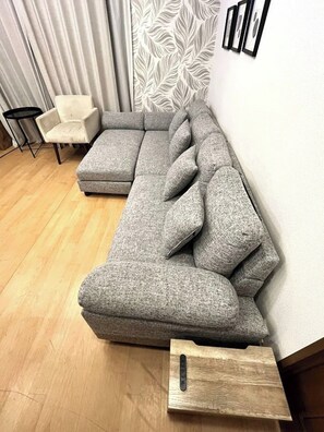 Un canapé modulable, accompagné d’une table d’appoint en bois, d’un fauteuil et d’un mur orné d’un motif.