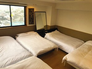 Une chambre d’hôtel avec trois lits simples, une grande fenêtre et un miroir fixé au mur.