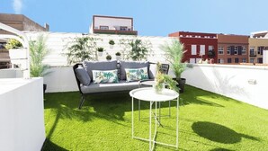 Terraza en la azotea con un sofá blanco, una mesita redonda y plantas en macetas.