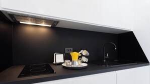 Una cocina moderna con encimera negra, estufa integrada, cafetera y lavamanos.