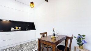 Una cocina moderna con armarios blancos, encimera negra y una mesa de comedor de madera con sillas. Una lámpara decorativa cuelga sobre la mesa, y hay una alfombra estampada en el suelo.